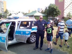 Policjant rozmawia z dziećmi przed radiowozem.