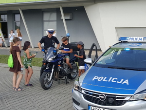 Policjant  umożliwia i pomaga wsiąść dzieciom na policyjny motocykl.