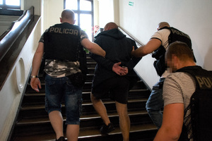 dwóch policjantów prowadzi po schodach zatrzymanego zakutego kajdankami