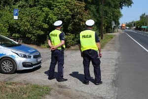 dwaj policjanci ruchu drogowego stoją obok radiowozu przy drodze