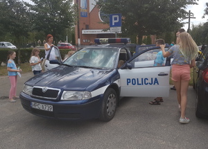 Młodzież ogląda policyjny radiowóz zaparkowany przed komisariatem na Wyżynach.