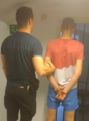 policjant trzyma zatrzymanego zakutego w kajdanki