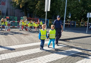 Policjanci ćwiczą z dziećmi przechodzenie przez przejście dla pieszych w rejonie szkoły.