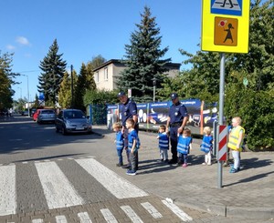 Policjanci przechodzą z przedszkolakami przez przejęcie dla pieszych.