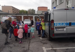 Dzieci oglądają policyjny radiowóz zaparkowany przed komisariatem.