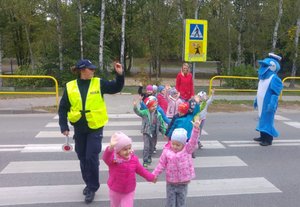 Dzieci ćwiczą przechodzenie przez jezdnię pod okiem policjantów i polfinka.