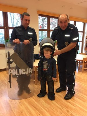 Policjanci pomagają dziecku ubrać elementy policyjnego umundurowania i wyposażenia.