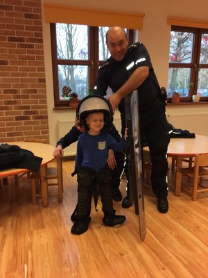 Dziecko ubiera elementy policyjnego umundurowania i wyposażenia. Pomaga mu policjant.