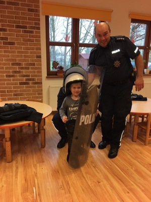 Dziecko ubrane w elementy policyjnego umundurowania i wyposażenia pozuje do zdjęcia w towarzystwie policjanta.