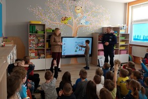 Zajęcia z dziećmi w sali przedszkolnej. Jedno z dzieci stoi przy ekranie telewizora i pokazuje na elementy wyświetlane na prezentacji multimedialnej.