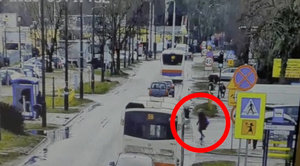 Kobieta przechodzi w miejscu niedozwolonym przez jezdnię tuż przez przejeżdżającym autobusem.