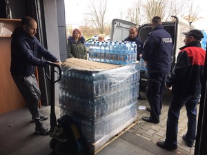 kilka osób, w tym policjanci pomagają przenieść z magazynu palety z wodą