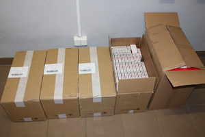 5 zabezpieczonych kartonów z nielegalnymi papierosami leżą na podłodze. Jeden karton jest otwarty