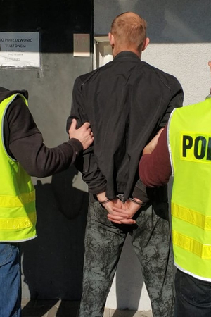 policjanci trzymają zatrzymanego skutego kajdankami