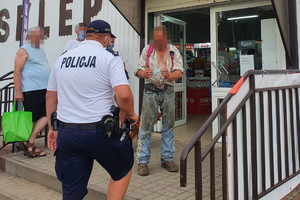 policjant wchodzi do sklepu. Obok stoją osoby. Jeden z mężczyzn zakłada maseczkę ochronną