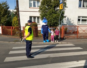 dzieci ćwiczą przechodzenie przez jezdnię pod okiem policjanta oraz polfinka