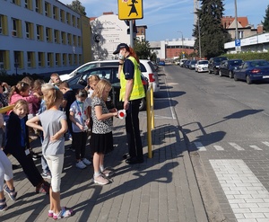 Policjantka rozmawia z dziećmi przy przejściu dla pieszych.