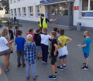 Policjantka rozmawia z dziećmi przez budynkiem szkoły.