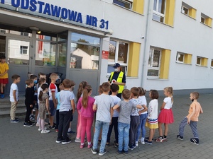 Policjantka rozmawia z dziećmi przez wejściem do budynku szkoły.