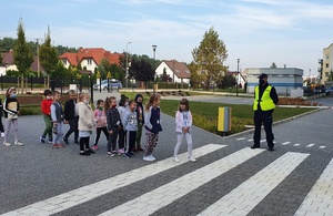 Policjant nadzoruje przechodzenie dzieci przez przejście dla pieszych