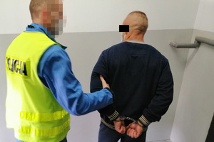 policjant trzyma zatrzymanego skutego kajdankami założonymi na ręce trzymane z tyłu