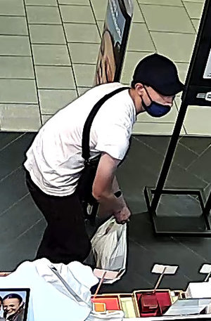 wizerunek pochylonego sprawcy kradzieży ubranego w białą koszulkę i czarne dresy. Na twarzy założoną niebieską maseczkę ochronną