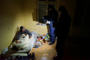 Policjanci rozmawiają z bezdomnym leżącym w łóżku.