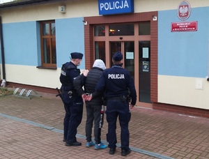 Policjanci prowadzą zatrzymanego przed budynkiem komisariatu w Białych Błotach.