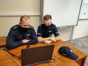 Policjanci siedzą w klasie szkolnej przy komputerze.