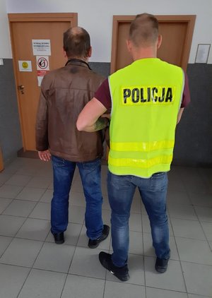 policjant prowadzi zatrzymanego korytarzem komisariatu