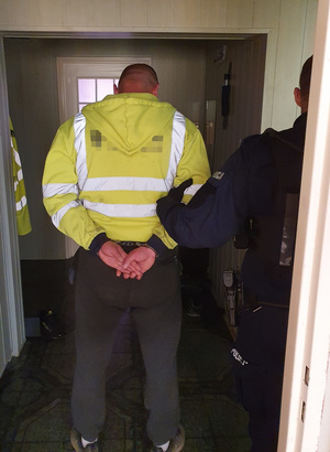 Policjant stoi  z zatrzymanym w jego mieszkaniu.