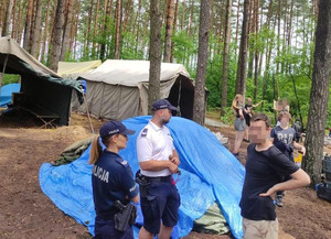 Policjanci kontrolują obozowisko. Po prawej stronie widoczni uczestnicy obozu.