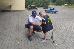 policjant pomaga założyć małemu chłopcu policyjną kamizelkę ratunkową