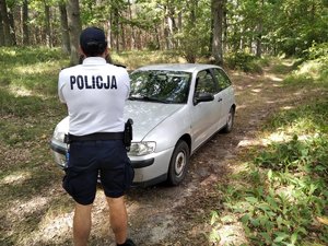 policjant stoi przed autem osobowym zaparkowanym w lesie
