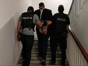 Policjanci prowadzą zatrzymanego po schodach.