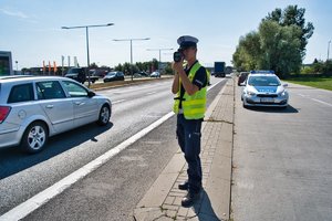 Policjant miernikiem prędkości mierzy prędkość pojazdów jadących ul. Jana Pawła II.