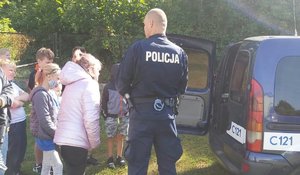 Policjant i dzieci stoją przy radiowozie od strony drzwi do strefy bagażowej auta.