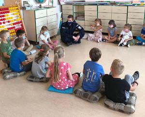 Policjant i dzieci siedzą w klasie szkolnej na podłodze podczas pogadanki.