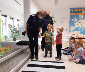Sala przedszkolna. Policjantka przeprowadza dzieci przez przejście dla pieszych w formie maty.