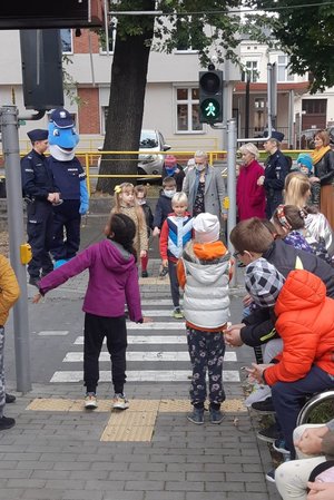 Uczniowie pod okiem policjantów, Polfinka i wychowawców przechodzą przez przejście dla pieszych z sygnalizacją świetlną znajdujące się na terenie ośrodka.