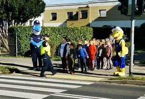 Policjanci z dziećmi i maskotkami stoją przy przejściu dla pieszych.