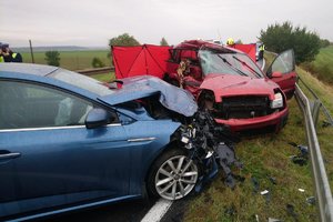 dwa rozbite auta koloru czerwonego i niebieskiego ustawione do siebie na przeciwko stoją przy barierkach