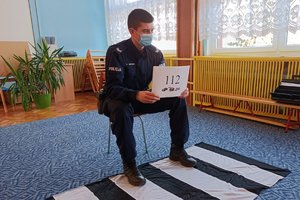 policjant siedzi na krześle i pokazuje kartkę z numerem alarmowym 112