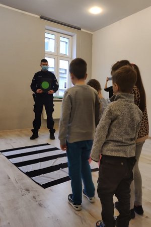 policjant pokazuje na kartce zielone światło dzieciom, które stoją przed imitacją przejścia dla pieszych