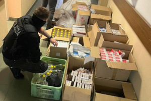 nieumundurowany policjant przegląda worki z krajanką tytoniową, butelki ze spirytusem oraz kartony z paczkami nielegalnych papierosów, które stoją na podłodze oparte o ścianę